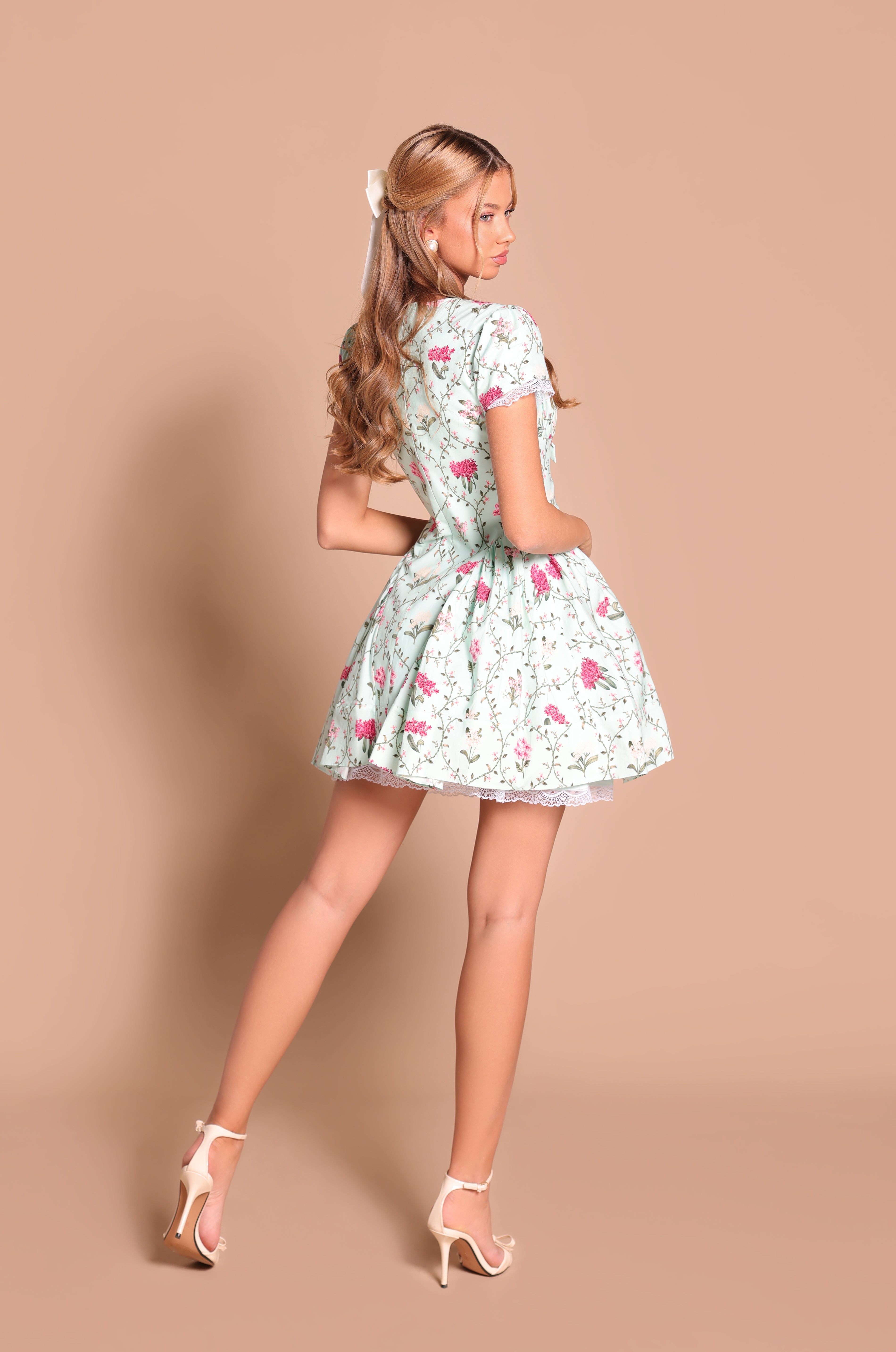A woman poses with her back partially turned, wearing the Mint Green Short Casual Dress: Analise and high heels against a plain beige background.